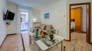 A dining area with a table set for two, a television mounted on the wall, and a balcony visible through an open door. - Casa Dolce Casa Central Stresa Apt 50m from lake, Stresa, Italy (Stresa)