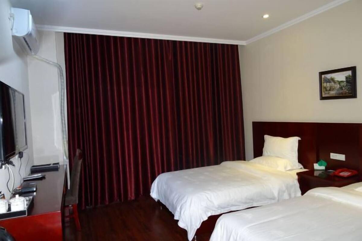 A hotel room with two beds, a TV, and a large window with curtains.