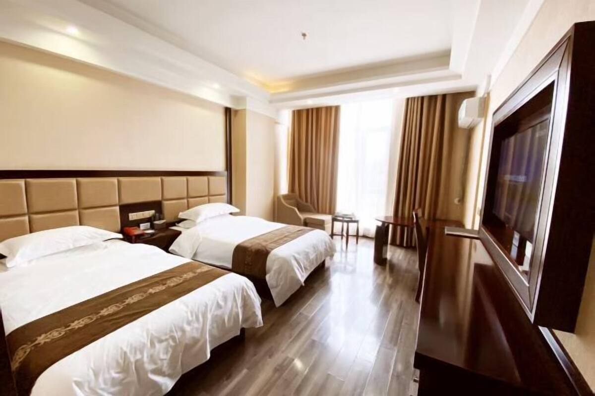 A hotel room with two beds, a TV, a desk, and a chair.