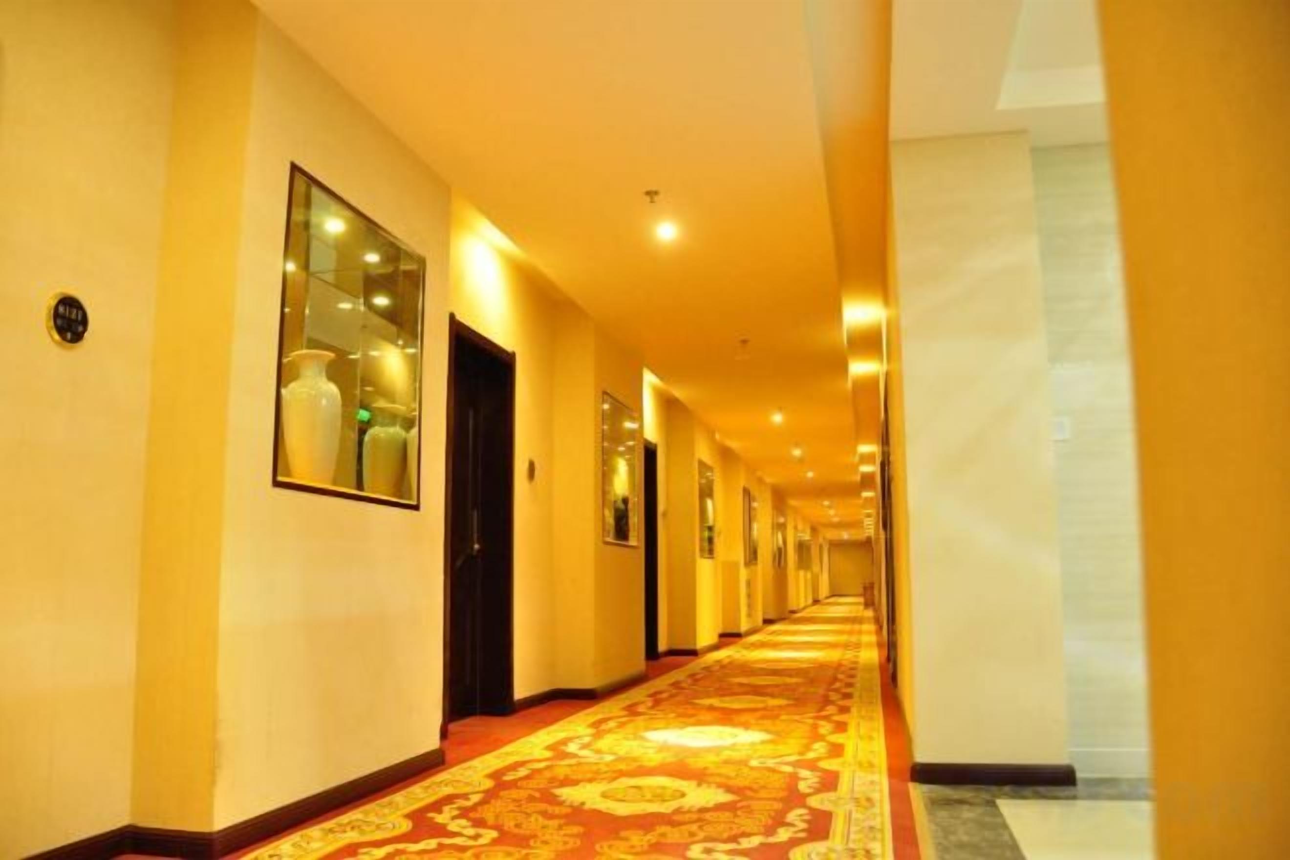 Un pasillo de hotel con alfombra estampada, puertas e imágenes enmarcadas en las paredes.