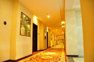 Un pasillo de hotel con alfombra estampada, puertas e imágenes enmarcadas en las paredes.