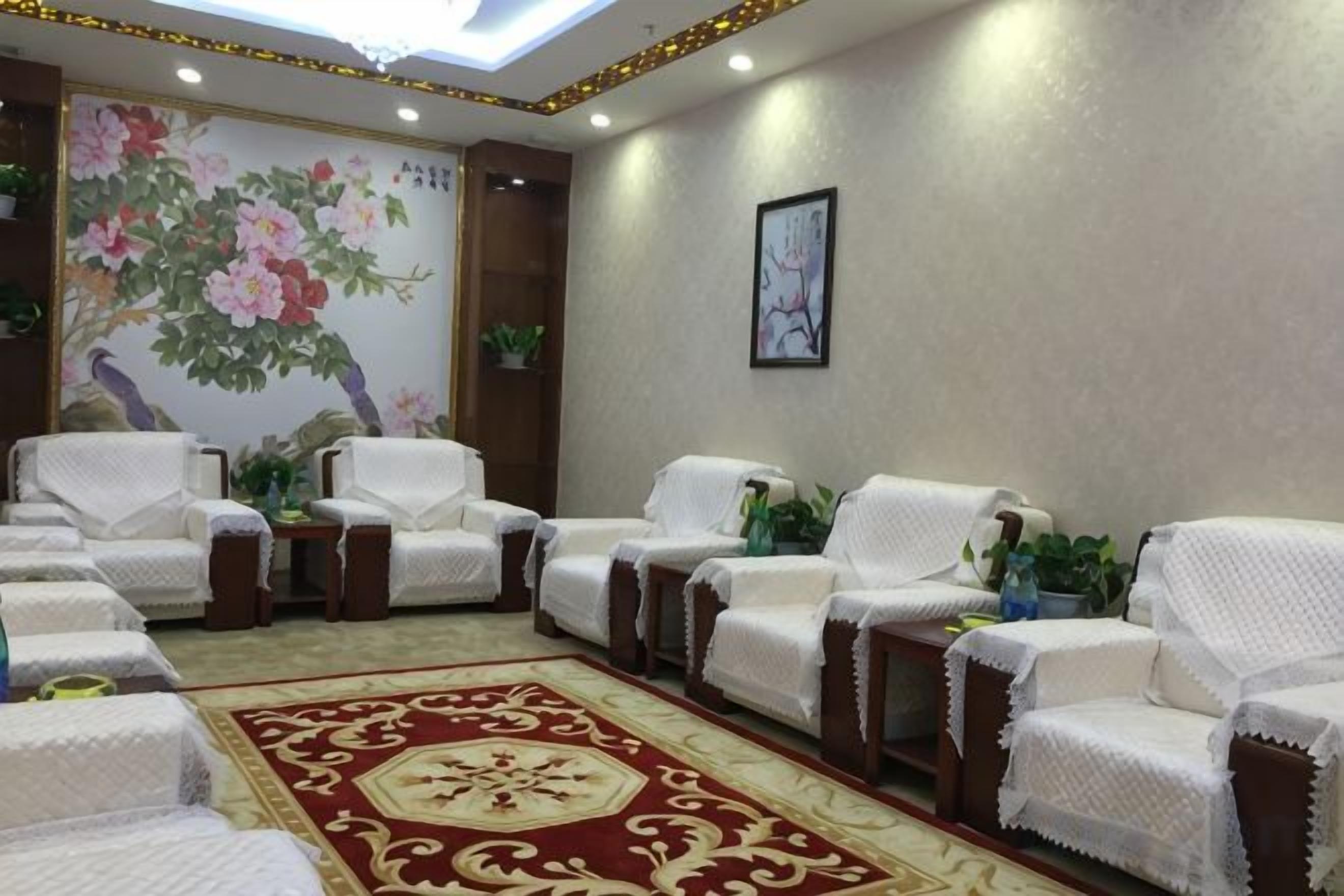 Una habitación con varias sillas blancas, una alfombra de diseño rojo y un cuadro con motivos florales en la pared.