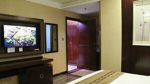Hotellihuone, jossa on sänky, jalustalla oleva televisio, vaatekaappi ja ovi, joka johtaa toiseen huoneeseen.