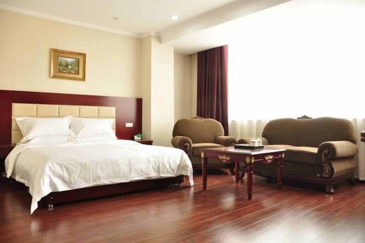 A hotel room with a bed, a sofa, a chair, a small table, and a painting on the wall.