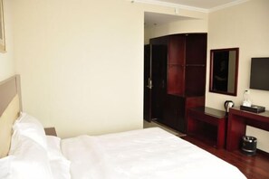 A hotel room with a bed, a wooden wardrobe, a desk with a mirror, and a television.