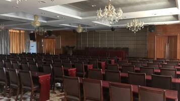 Un salón de conferencias con filas de sillas y mesas, una araña y una zona de escenario.