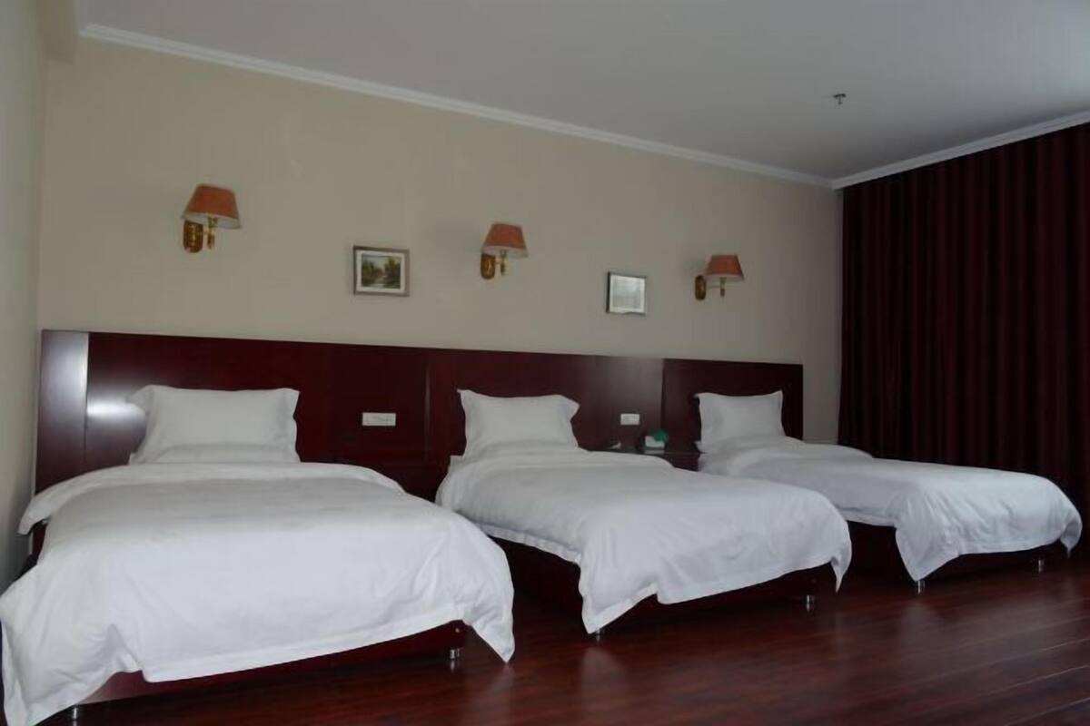 A hotel room with three single beds, a wooden headboard, and wall-mounted lamps.