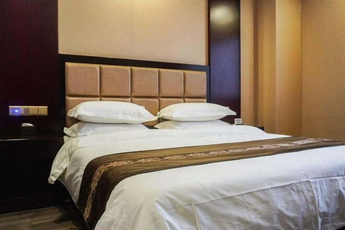 A hotel room with a large bed, a nightstand, and a wall-mounted light.