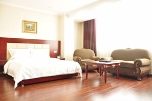 A hotel room with a bed, two armchairs, a wooden coffee table, and a painting on the wall.
