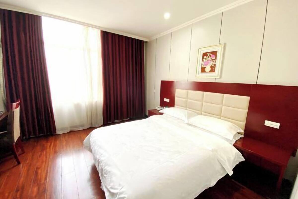 A hotel room with a large bed, a wooden floor, a nightstand, and a window with curtains.