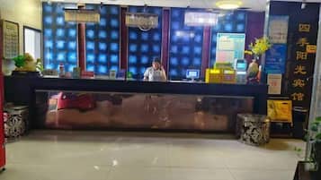 A hotel reception desk with a digital screen, a receptionist, and a decorative wall.