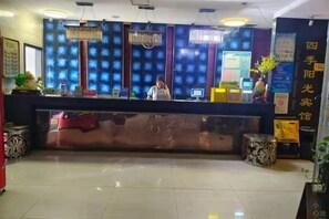 Una recepción de hotel con una pantalla digital, una recepcionista y una pared decorativa.