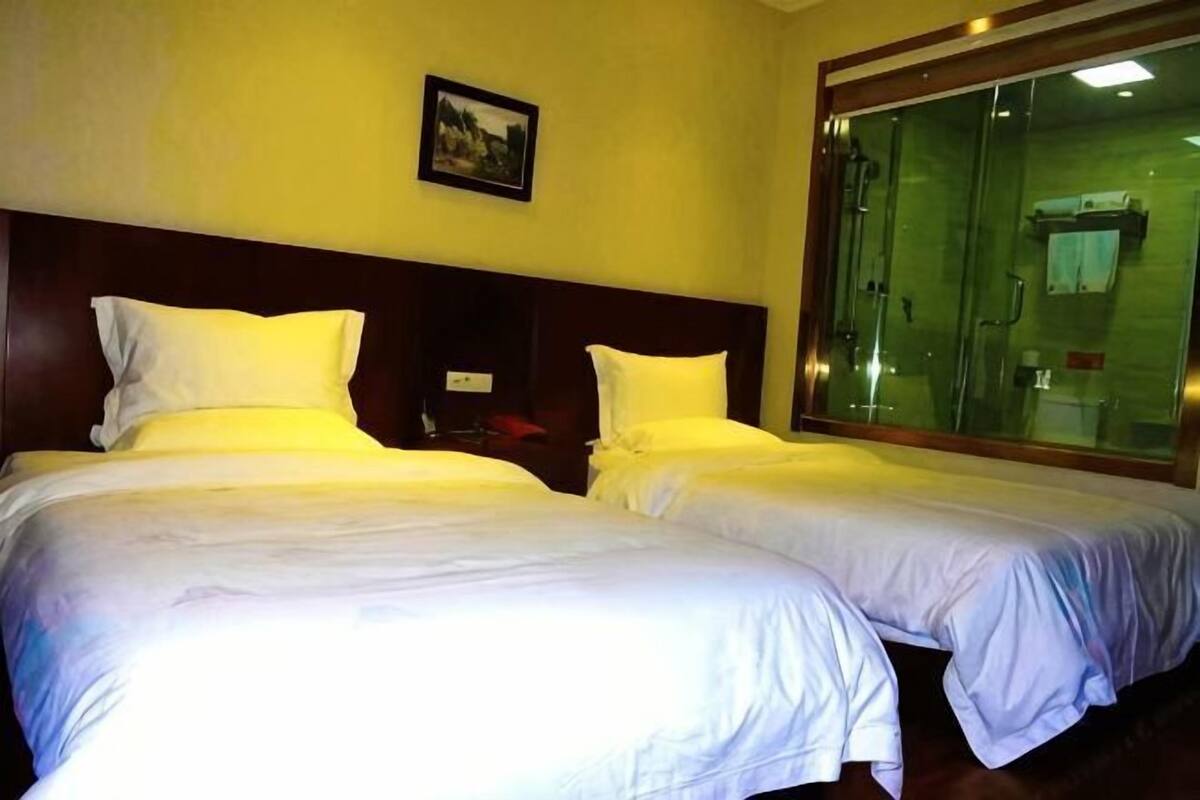A hotel room with two beds, a wooden headboard, a large window, and a picture on the wall.
