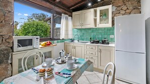 A kitchen with stone walls, wooden ceiling, white cabinets, a sink, and a table set for breakfast.