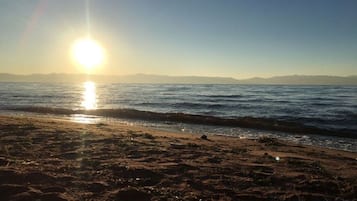 Una playa con cielo despejado y el sol poniéndose sobre el agua.