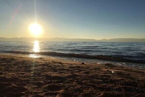 Une plage avec un ciel dégagé et le soleil se couchant sur l’eau.