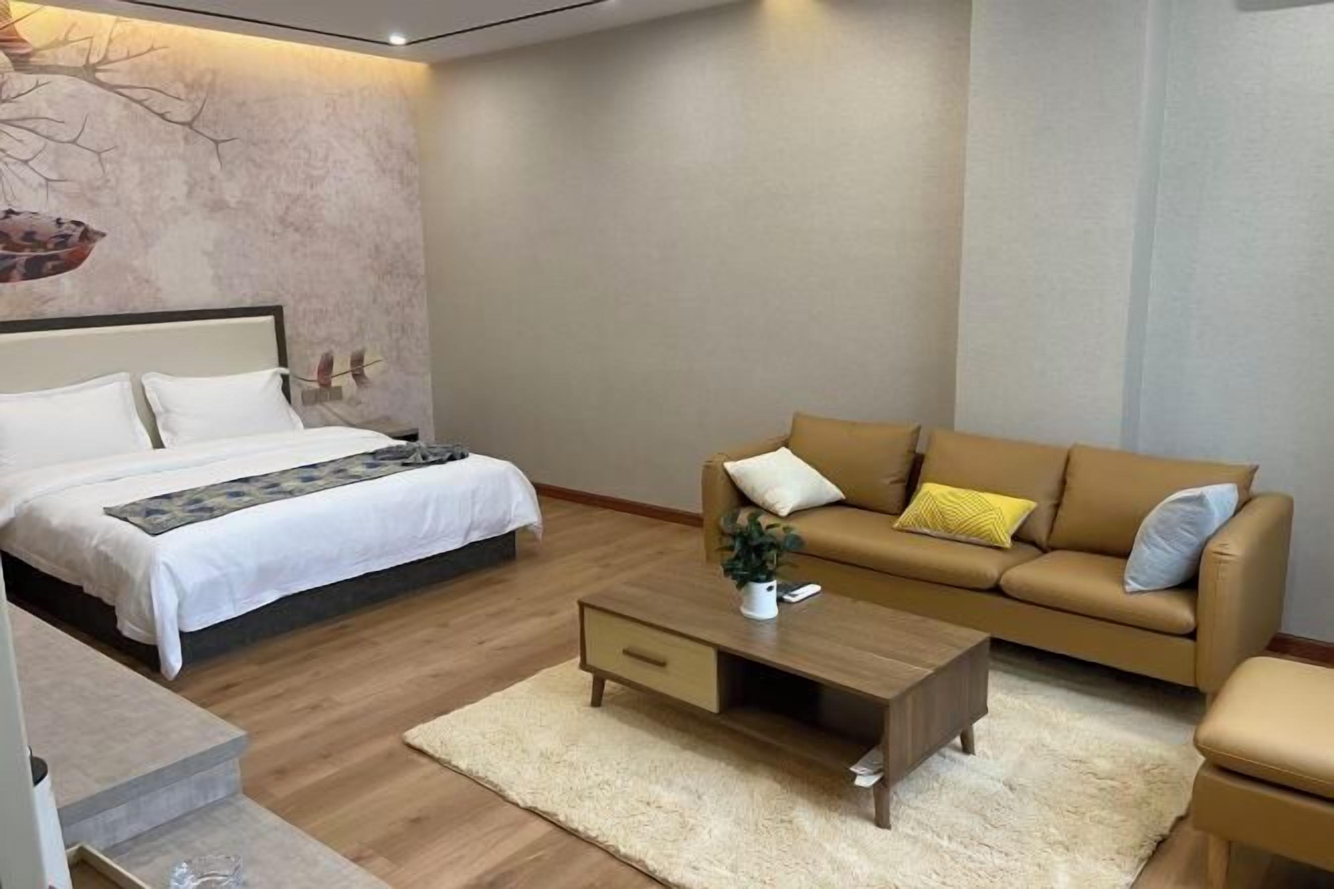 A bedroom with a bed, a sofa, a coffee table, and a wall with a tree and bird mural.