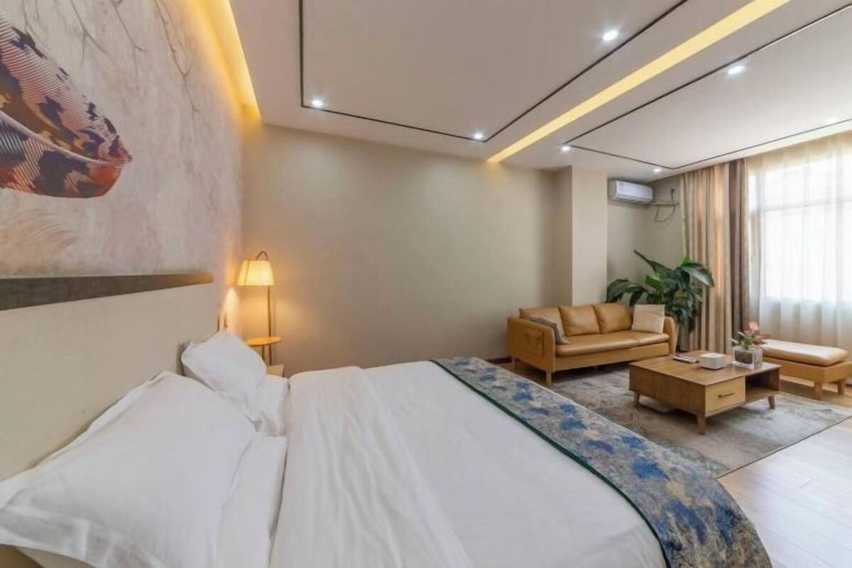 A hotel room with a bed, a sofa, a coffee table, a lamp, and a painting on the wall.