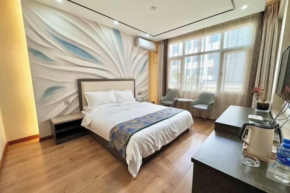 Ein Hotelzimmer mit Bett, Schreibtisch, Stuhl und einem fenster mit Vorhängen.
