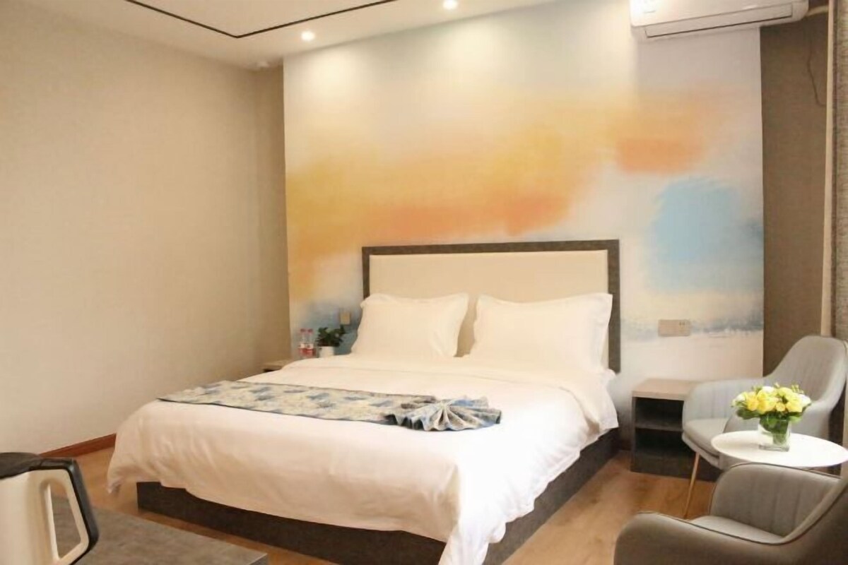 A hotel room with a large bed, a bedside table, a chair, and a wall with a painted landscape.