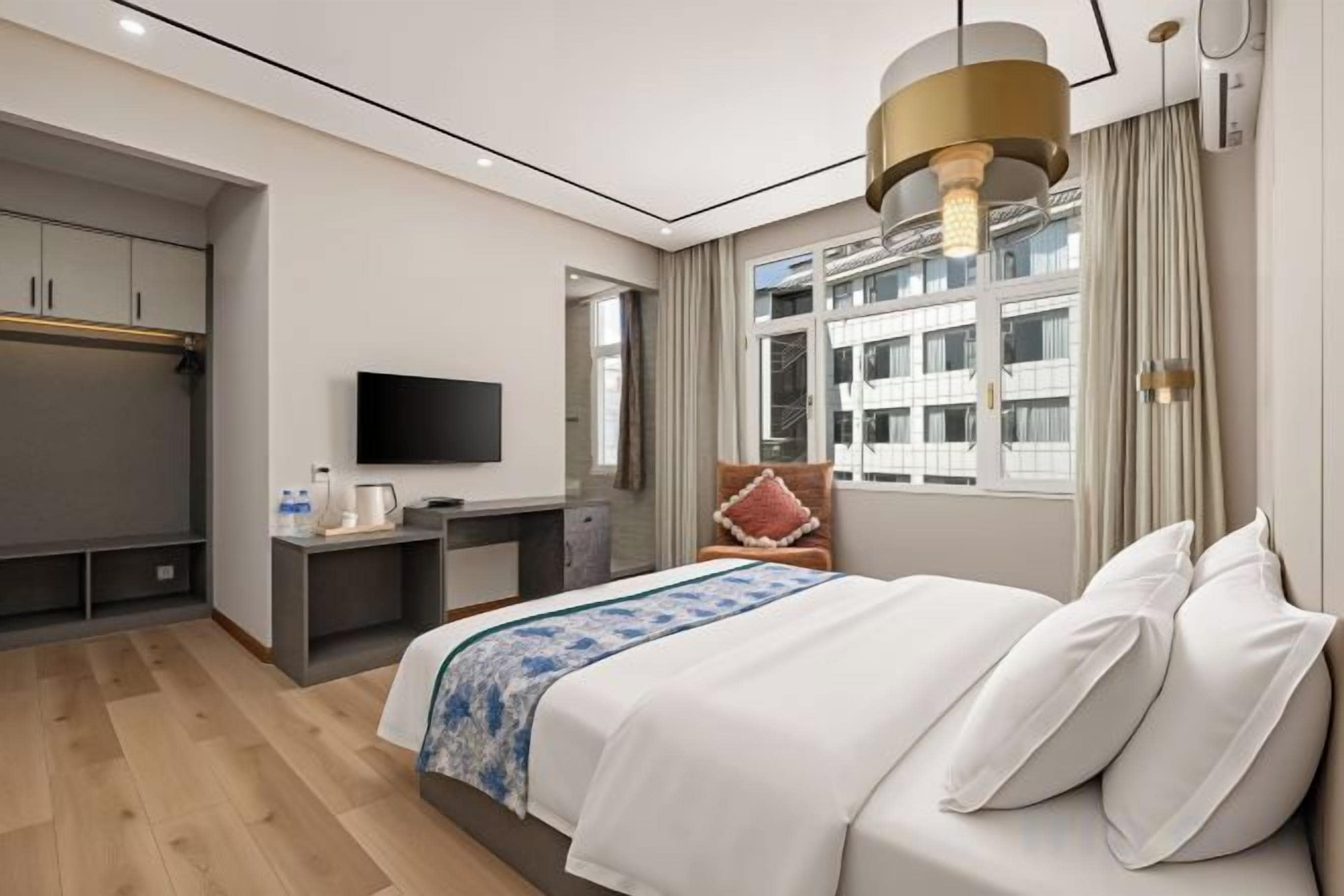 A hotel room with a bed, a desk, a television, and a window with a view of buildings.