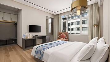 A hotel room with a bed, a desk, a television, and a window with a view of buildings.
