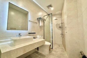 A modern bathroom with a large mirror, a sink, a toilet, and a glass-enclosed shower. - Noah Hotel (Chengjiang)