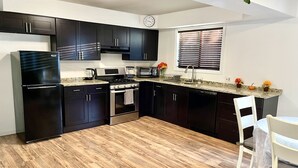 A modern kitchen with dark cabinets, stainless steel appliances, a wooden floor, and a window with blinds. - Homey, Cheerful & Spacious🙂 (Clifton)