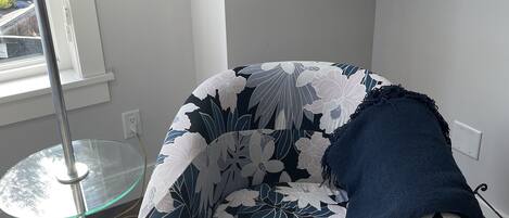 A corner room with a floral-patterned armchair, a glass table, and a lamp.