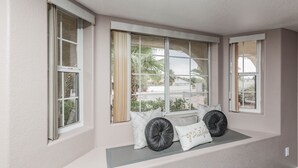 A room with a built-in bench under a large window, offering a view of palm trees and a house. - Private Vegas Executive Home 15 Min To Strip Quiet Neighborhood (Las Vegas)