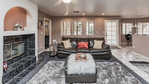 A living room with a fireplace, a black leather sofa, a fluffy ottoman, and a ceiling fan. - Private Vegas Executive Home 15 Min To Strip Quiet Neighborhood (Las Vegas)