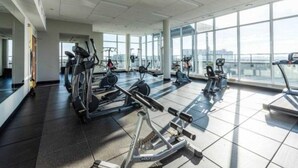 Uma academia ampla com diversos equipamentos de exercício, grandes janelas e teto alto.