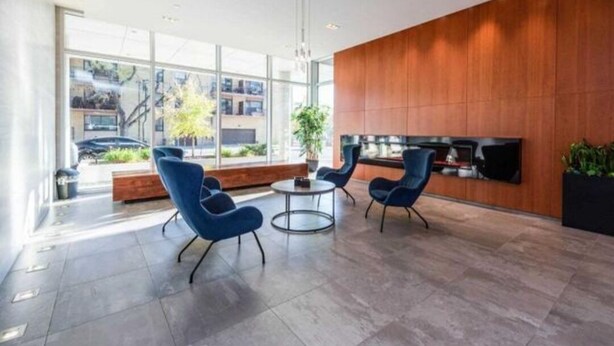 Um lobby moderno com parede de destaque em madeira, janelas amplas e cadeiras azuis.