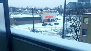 Vista de uma estação de metro com um estacionamento coberto de neve e edifícios ao fundo.