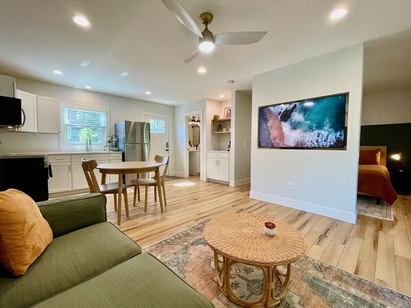 A modern living room with a sofa, a dining table, and a TV mounted on the wall.