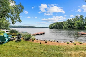 A lakeside property with a dock, green chairs, and a grassy area.