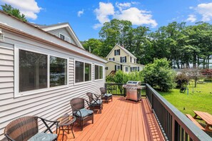 Une terrasse dotée de mobilier d’extérieur et d’un barbecue, entourée d’une cour clôturée et d’arbres.