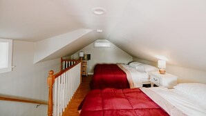 Une chambre avec deux lits, un escalier en bois et une table de chevet blanche avec une lampe.