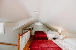 A bedroom with two beds, a wooden staircase, and a white nightstand with a lamp. - Little Landing Cottage | Lakefront · Dock · Kayaks (Winthrop)