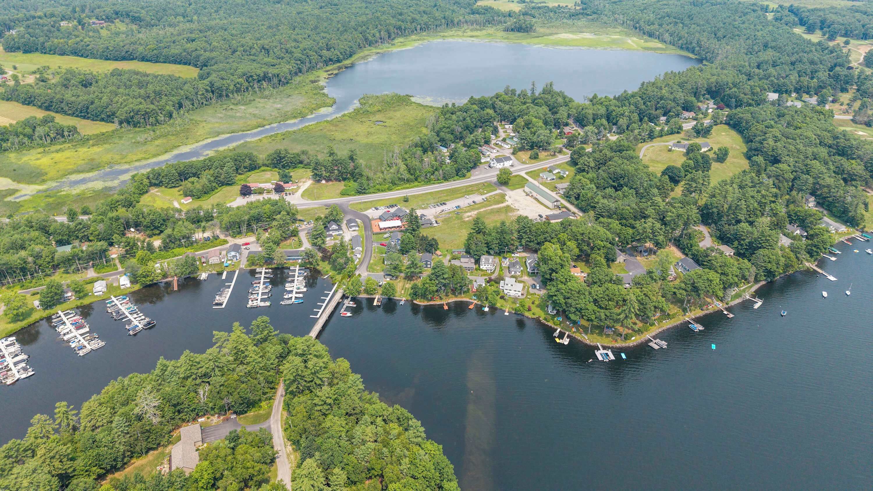 Vue aérienne d’une propriété située au bord d’un lac, avec un port de plaisance, des bâtiments et une végétation luxuriante.