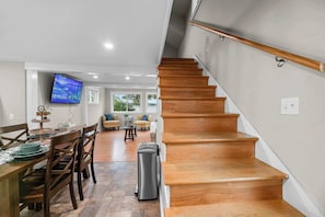 A modern interior with a wooden staircase, a dining area with a TV, and a view through the windows.