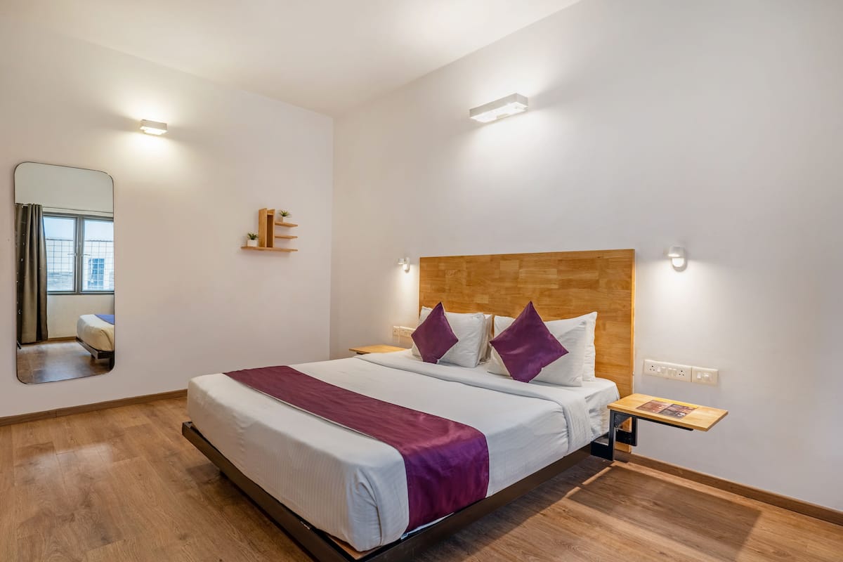 A neatly arranged hotel room with a large bed, a wooden headboard, a bedside table with a magazine, and a mirror on the wall.