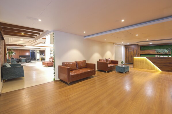 A spacious lobby with a wooden floor, leather sofas, and a reception desk with a green wall.