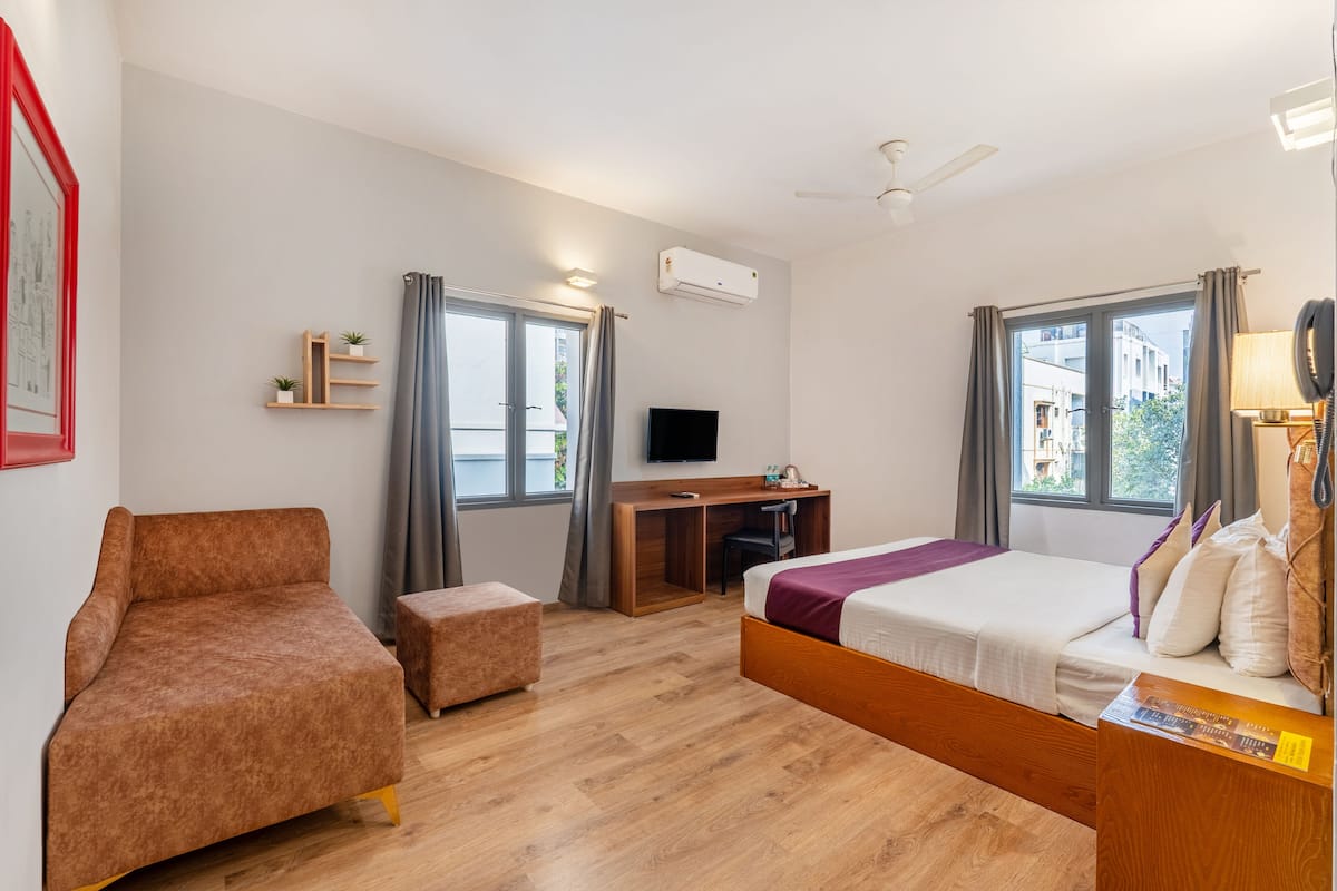 A modern hotel room with a sofa, a bed, a desk, and a TV.
