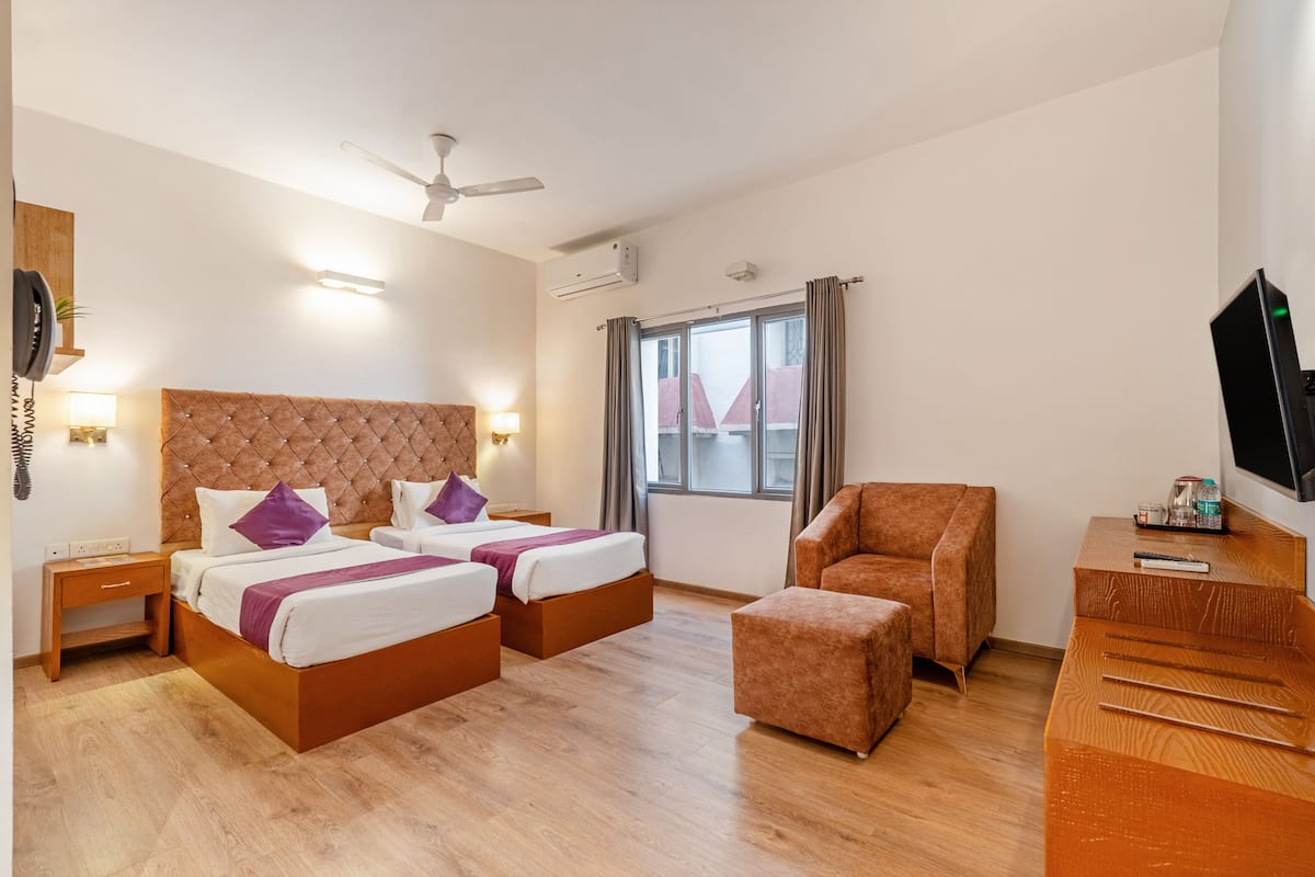 A hotel room with two beds, a sofa, a TV, and a window with curtains.