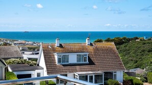 A coastal residential area with houses, a clear blue sky, and the sea in the background.