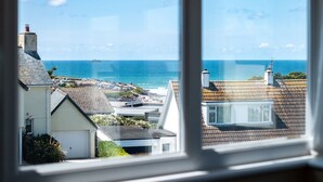 A coastal view from a window overlooking a residential area with houses and the sea.