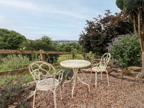 A garden patio with a round table and two chairs, surrounded by mulch and plants. - The Carriage (Lydney)