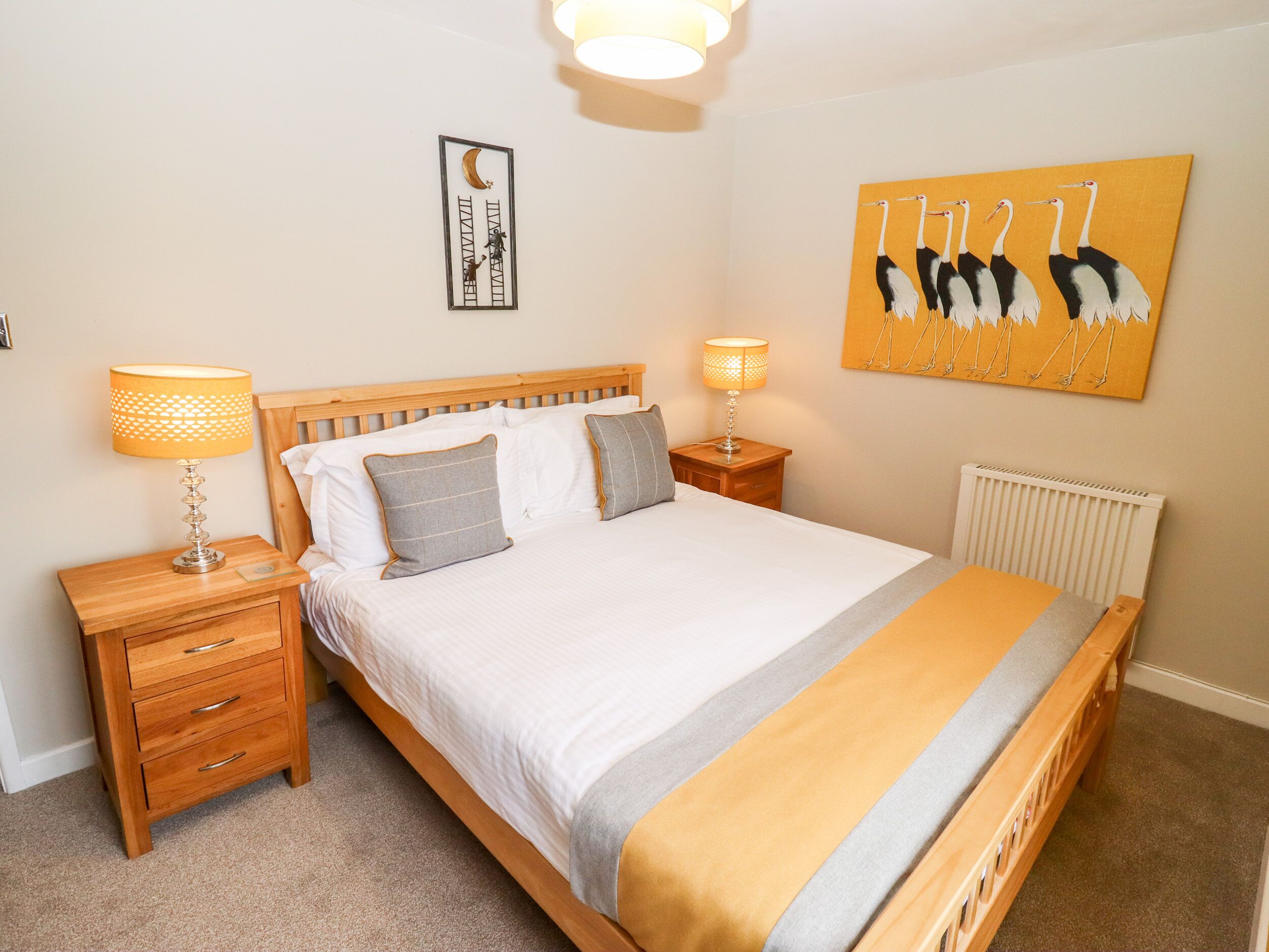 A neatly arranged bedroom with a wooden bed, two bedside tables with lamps, a wall-mounted artwork, and a radiator.