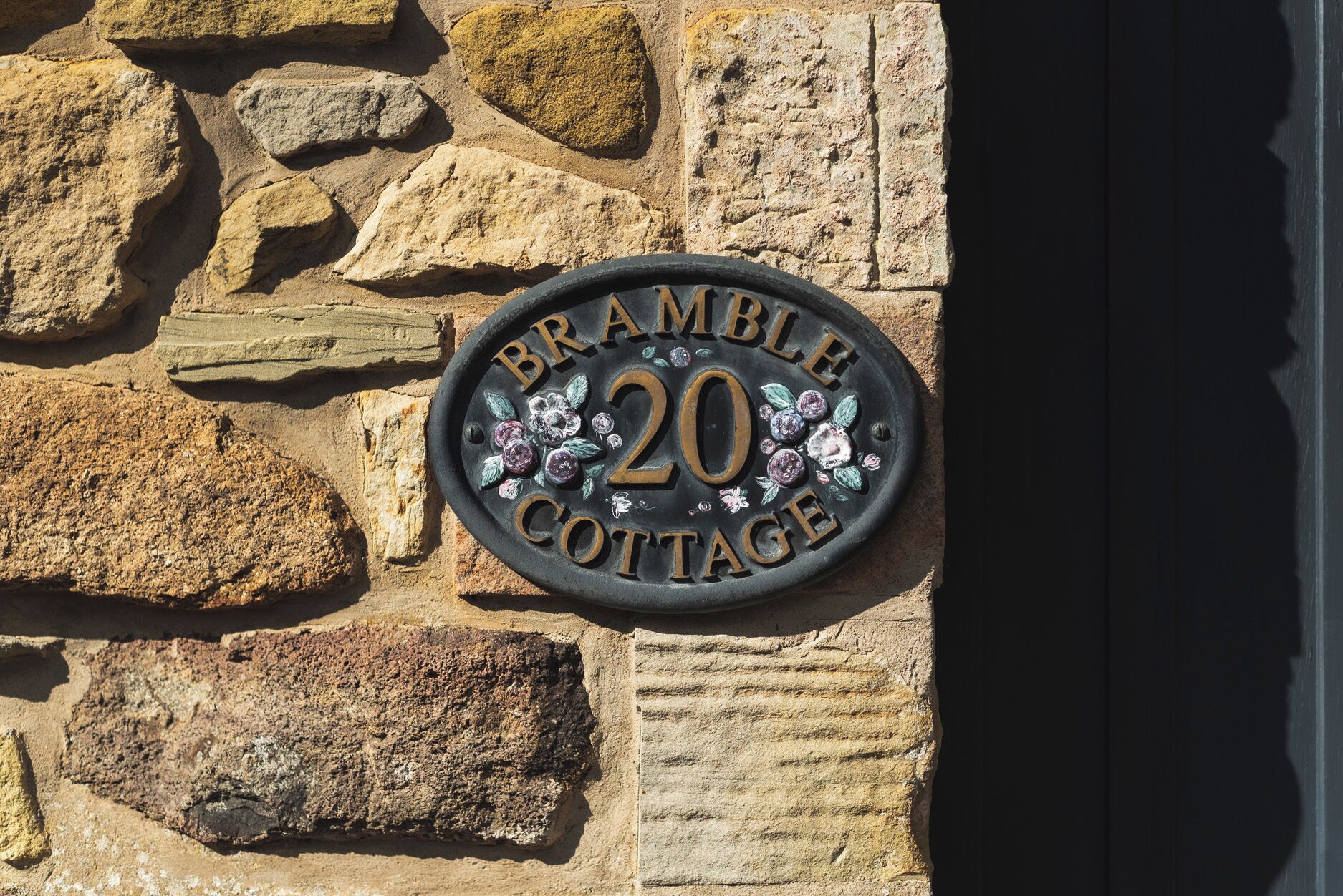 Un mur de pierres sur lequel est fixée une plaque métallique portant l’inscription « BRAMBLE COTTAGE 20 ».